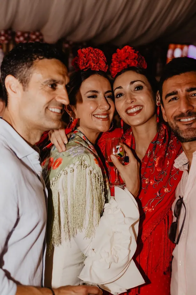 Dos mujeres con trajes de flamenca y flores en el pelo posando con dos amigos