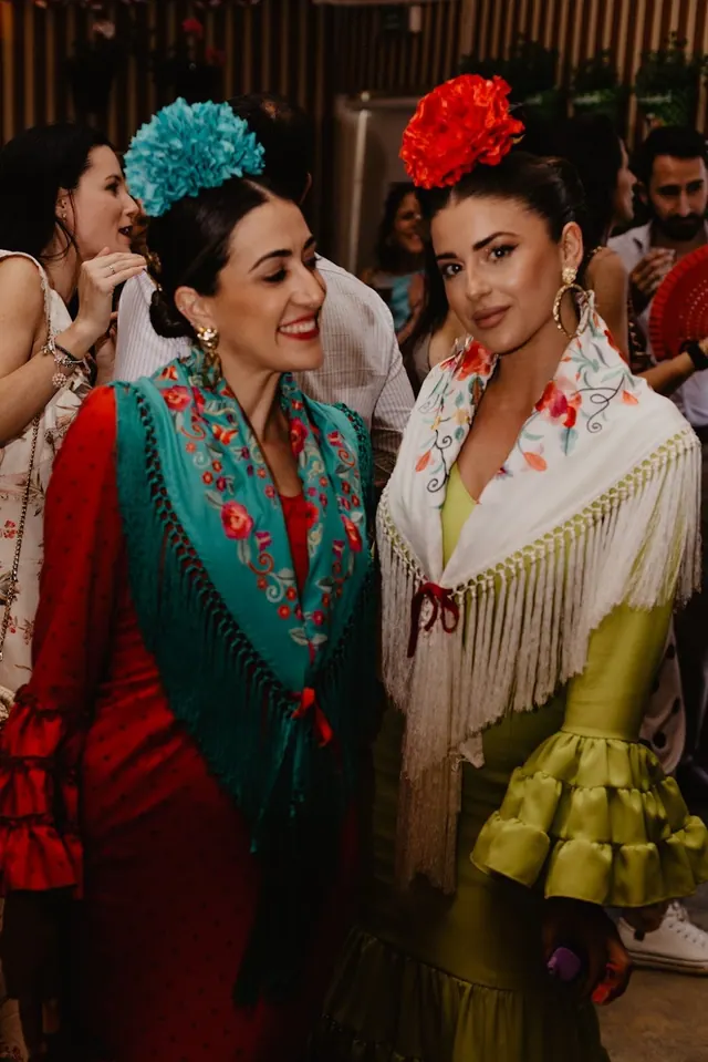 Dos mujeres con trajes de flamenca turquesa y verde, con flores en el pelo