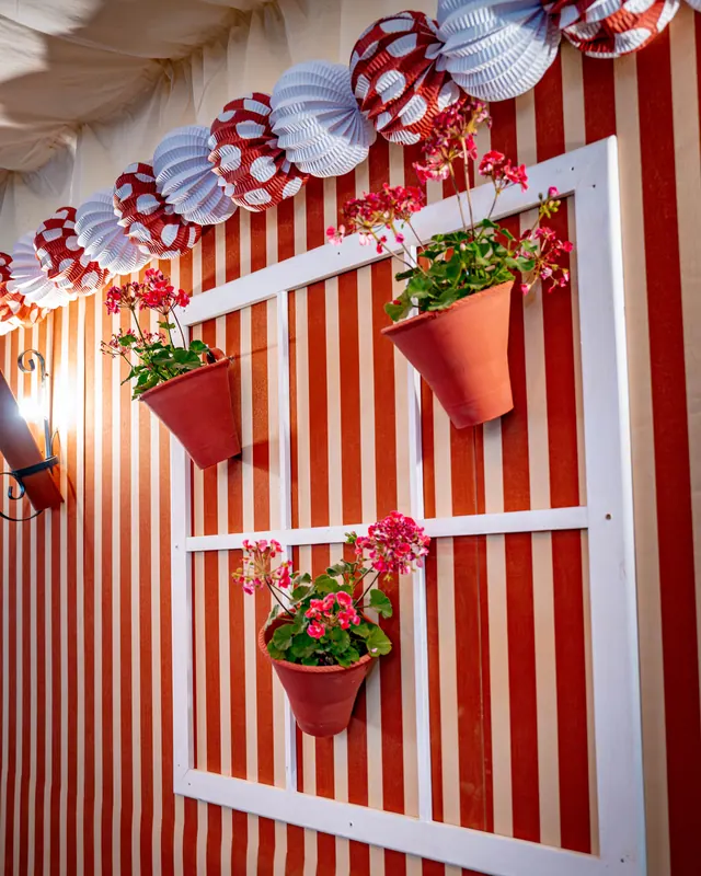 Pared de rayas rojas y blancas con maceteros de flores y farolillos de papel